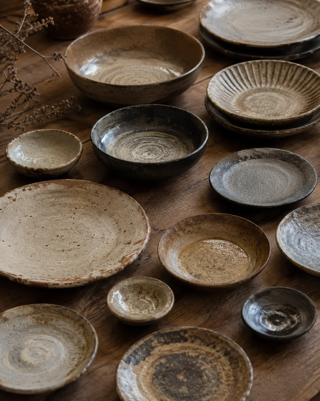 Plates and bowls arranged like a landscape of earth tones, revealing the depth of handmade ceramic surfaces.